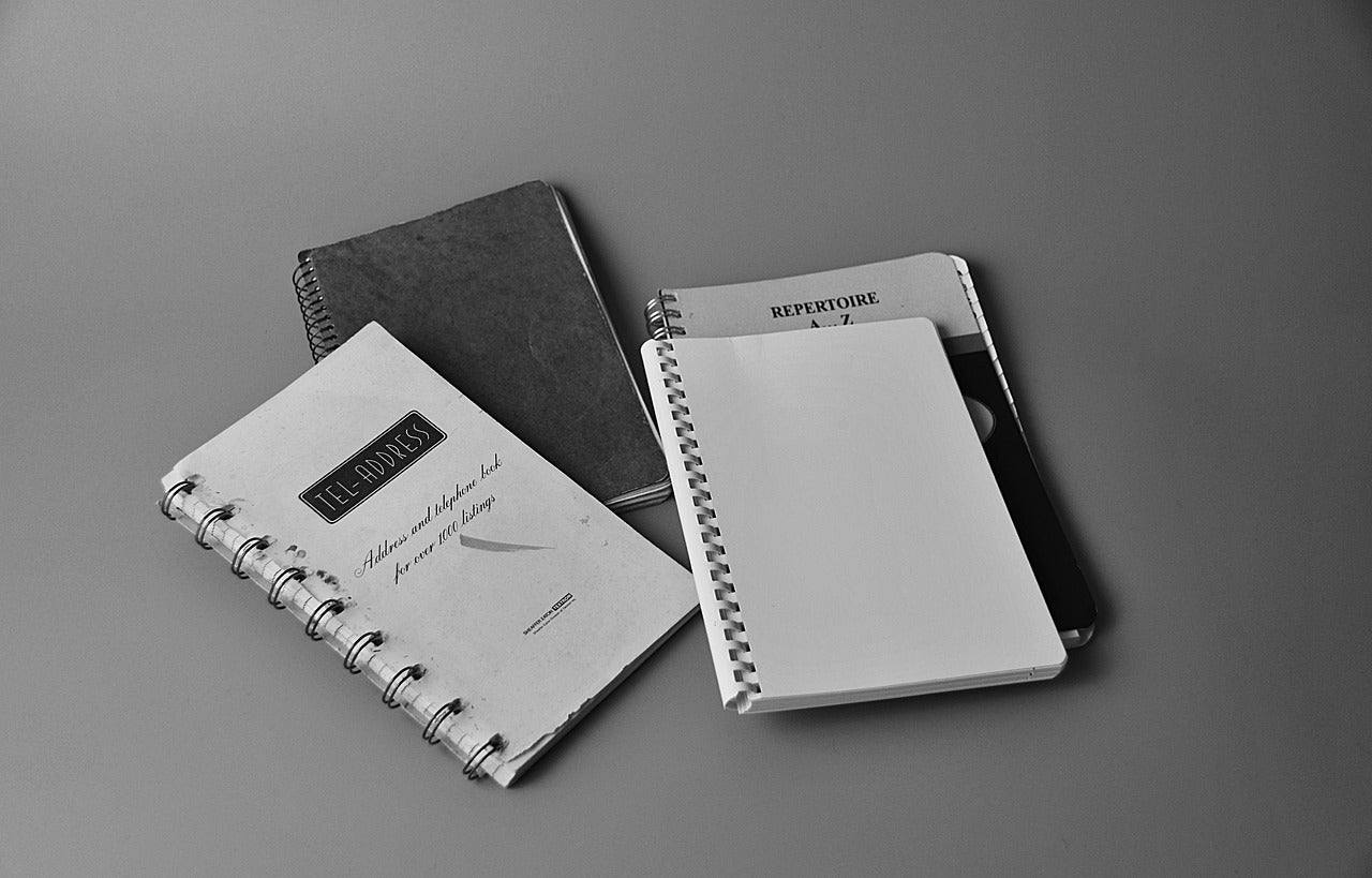 4 agendas avec couvertures blanches et noires, 2 ouverts et 2 fermés sur fond gris