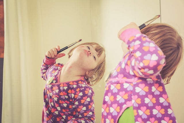 petite fille habillée en rose qui se maquille et se regarde dans le miroir 