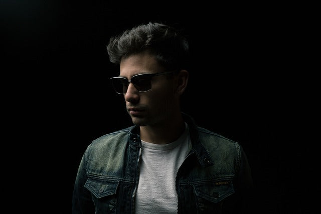 homme avec lunettes de soleil, veste kaki, t-shirt gris sur un fond noir