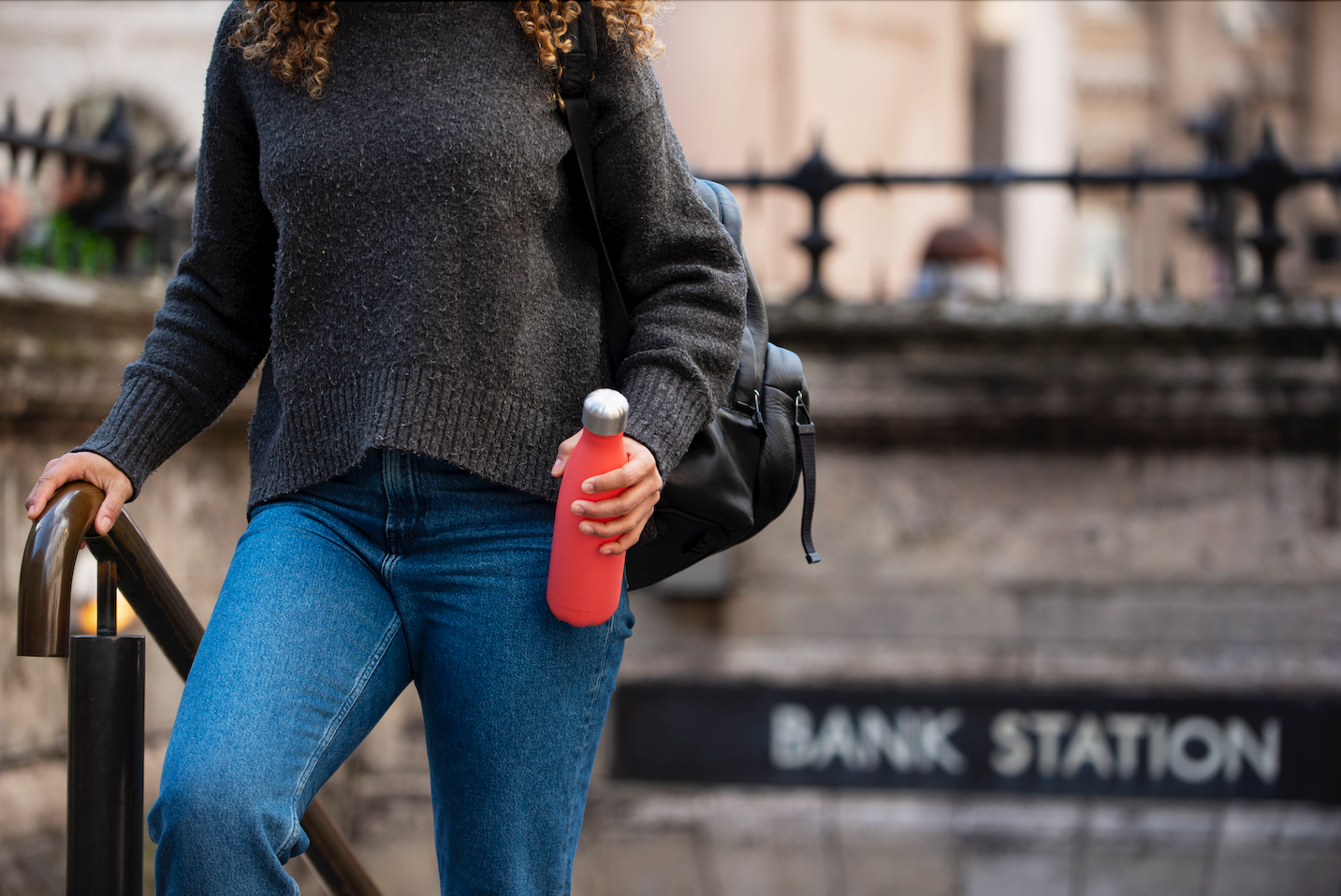 jeune femme sortant du metro tenant une gourde rouge dans sa main
