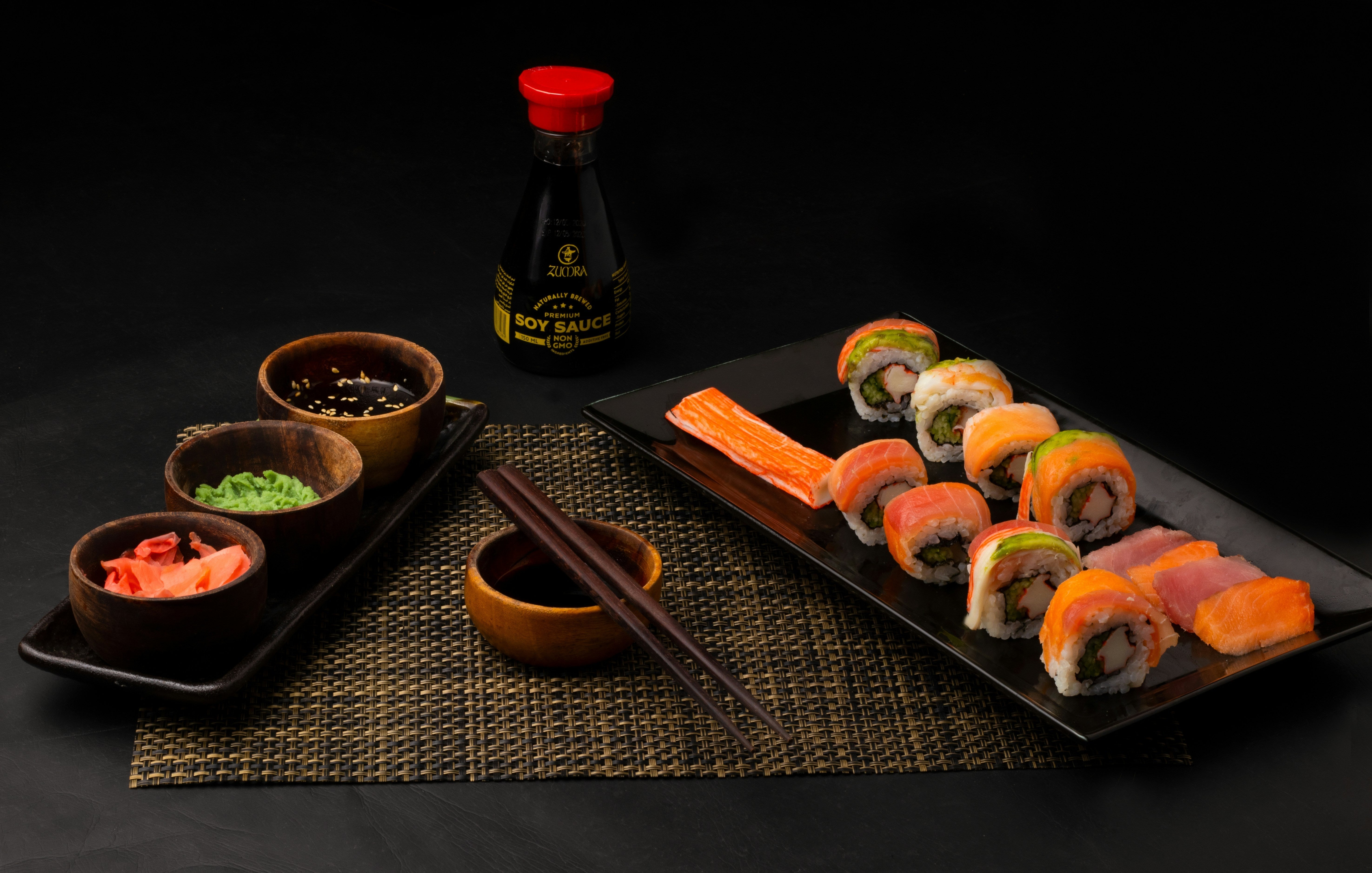sauce, wasabi, baguette, gingembre, et sushis sur un plateau sur une table noir 