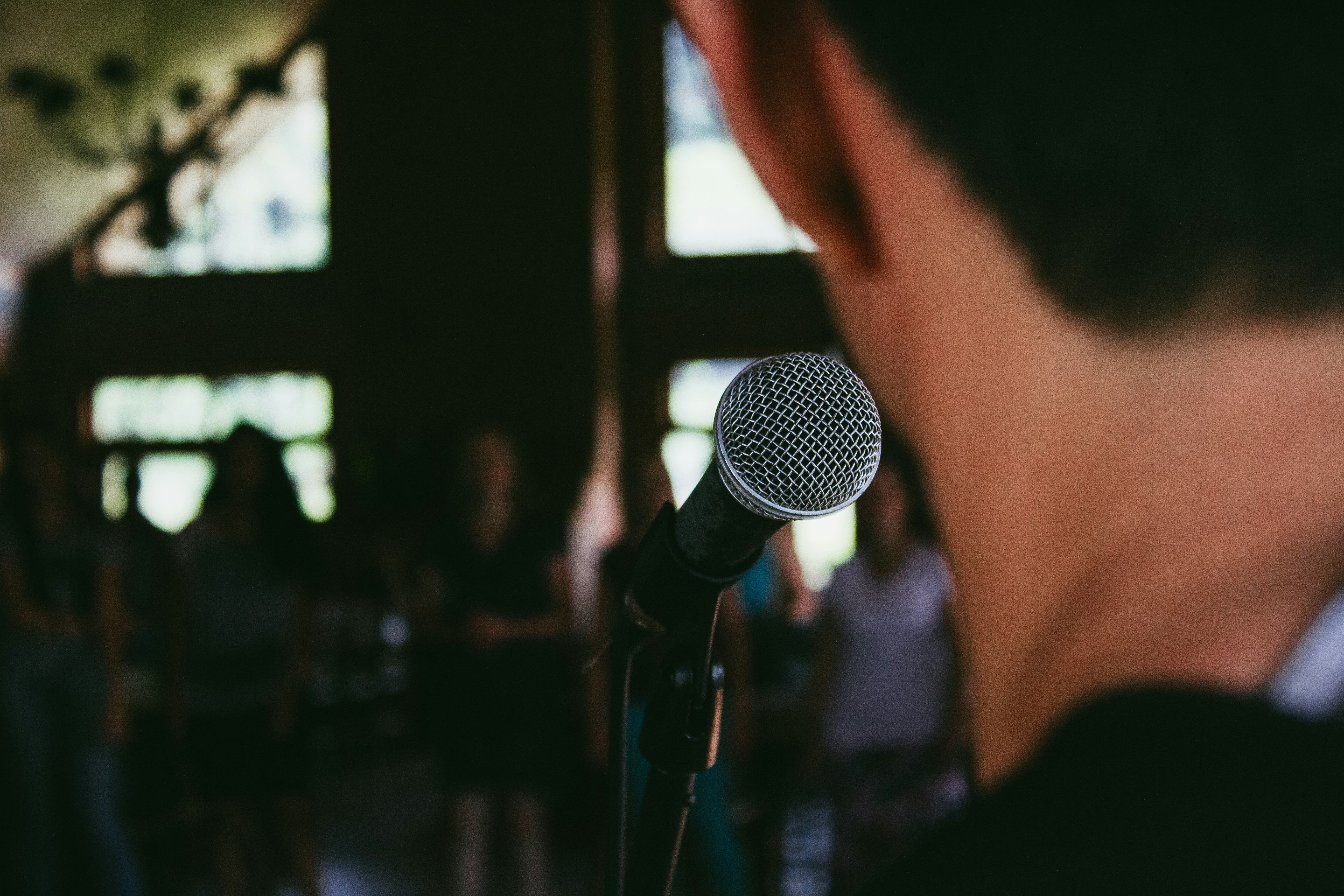 homme qui chante de dos, on y voit le haut de sa tête et le micro. En arrière plan : des personnes