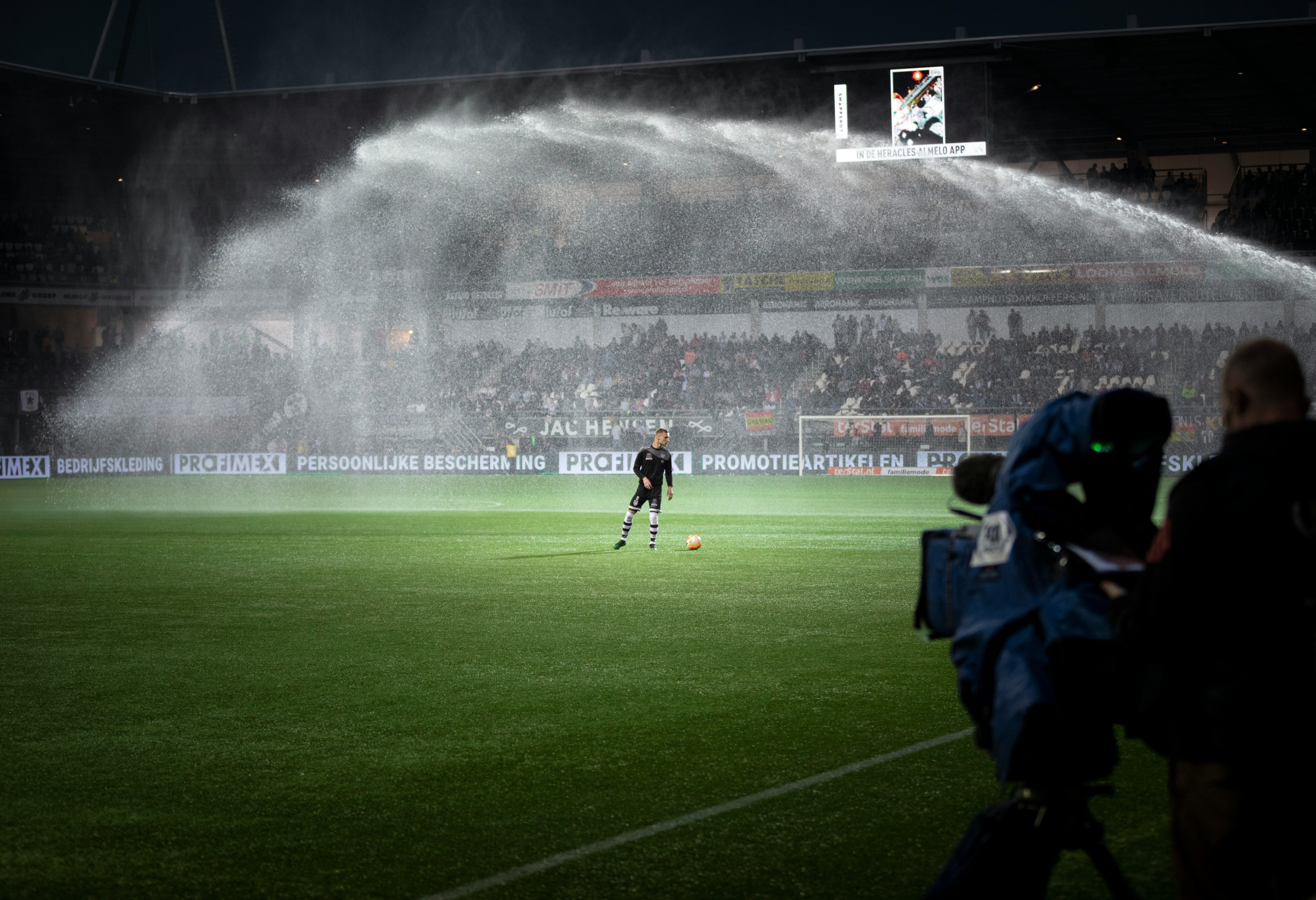 stade, qui se fait arroser, on y voit un joueur au milieu avec un ballon 