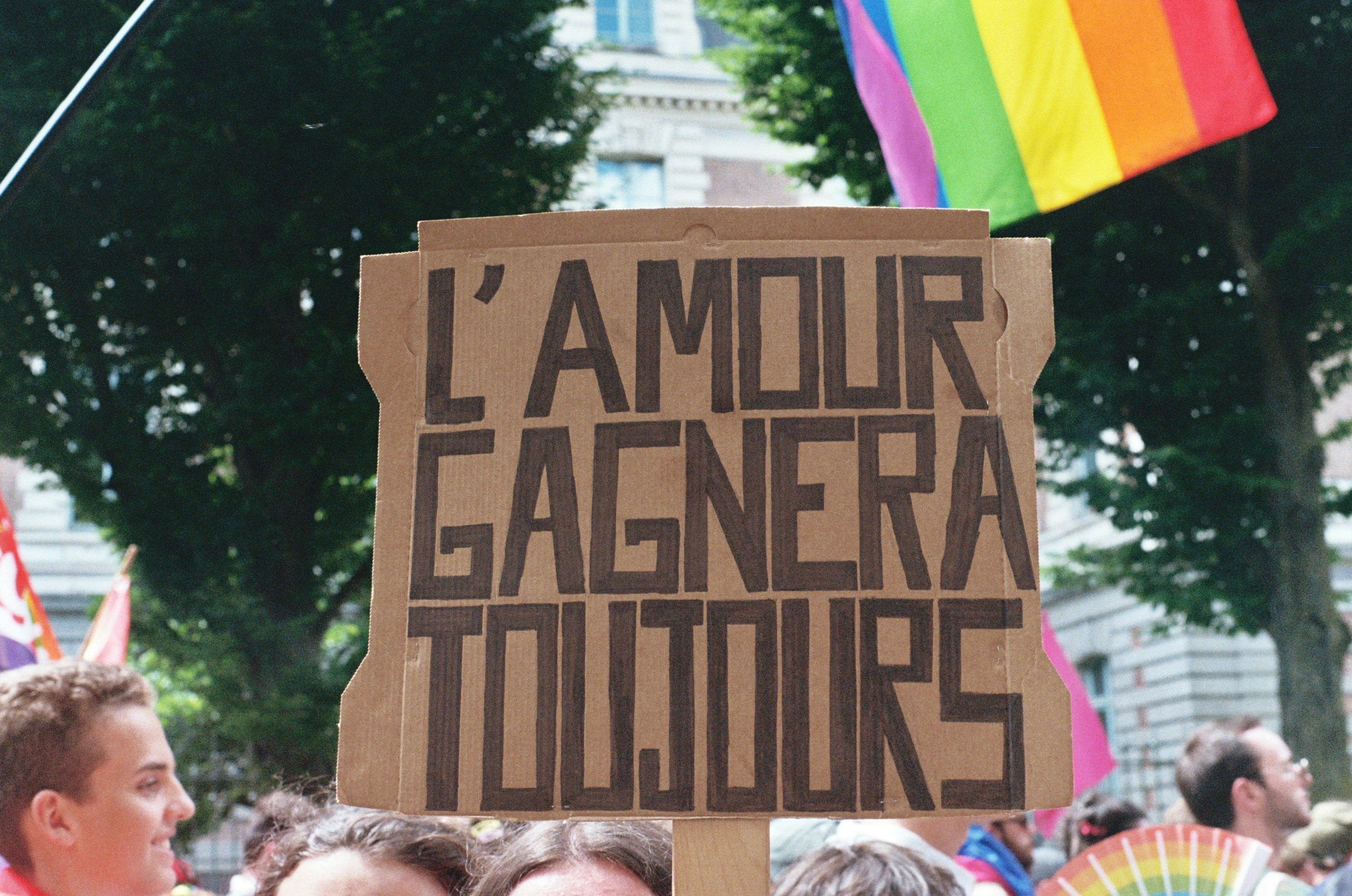 manifestation LGBTQIA + "l'amour gagnera toujours" écrit sur ne pancarte en carton avec des drapeaux 