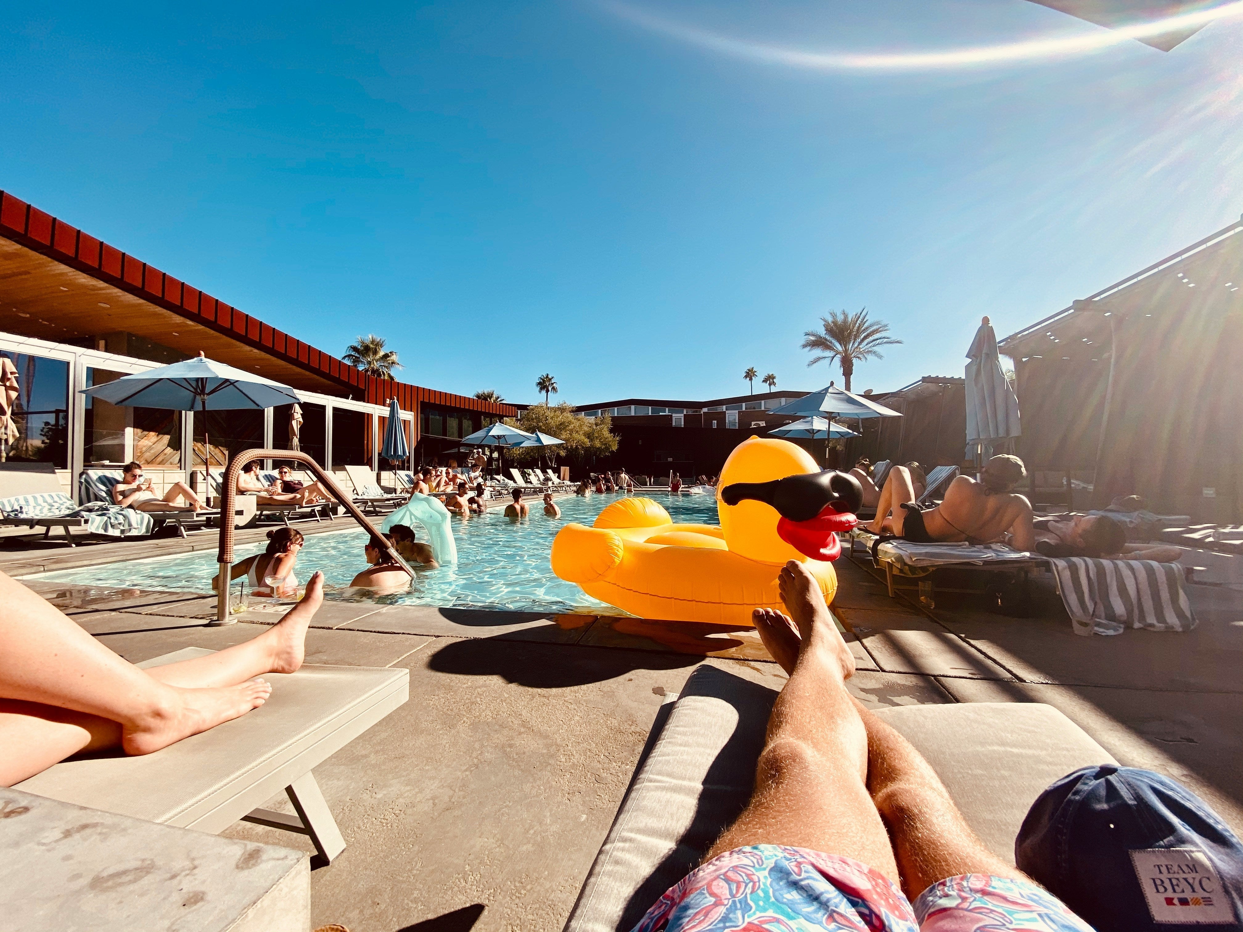 personnes sur des transats et dans la piscine, il y a des bouées, c'est sous le soleil 
