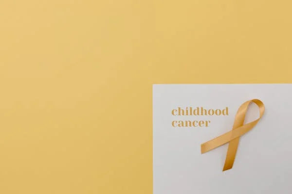 "childhood cancer" écrit sur une feuille blanche avec un ruban jaune et le signe du soutien contre le cancer - sur un fond jaune 