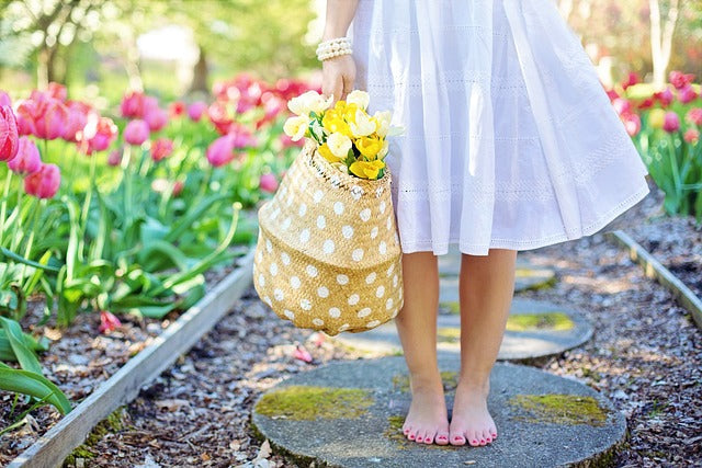 bas du corp d'une petite fille habillée en blanc, avec un panier en osier et des fleurs, elle est pied nu et il y a des tulipes roses autour