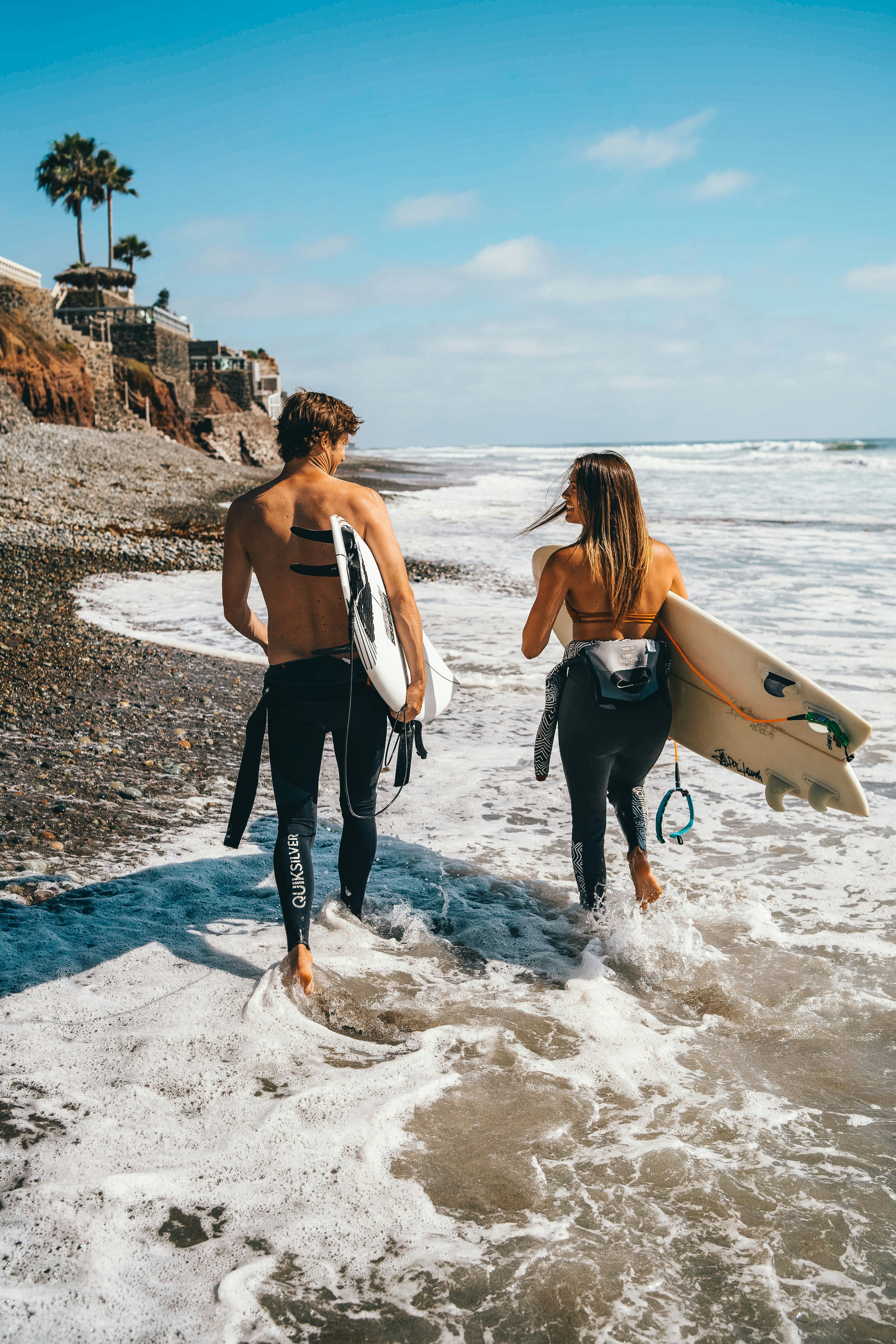 deux personnes qui marchent les pieds dans l'eau avec des planches de surf 