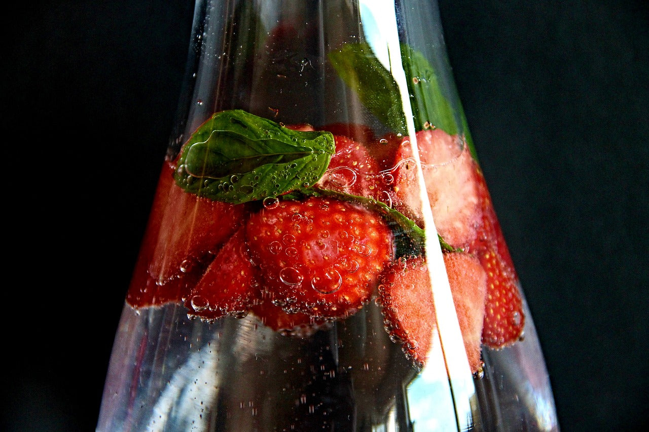 carafe transparente en verre contenant de l'eau avec de la fraise et des feuilles de menthe dedans sur fond noir
