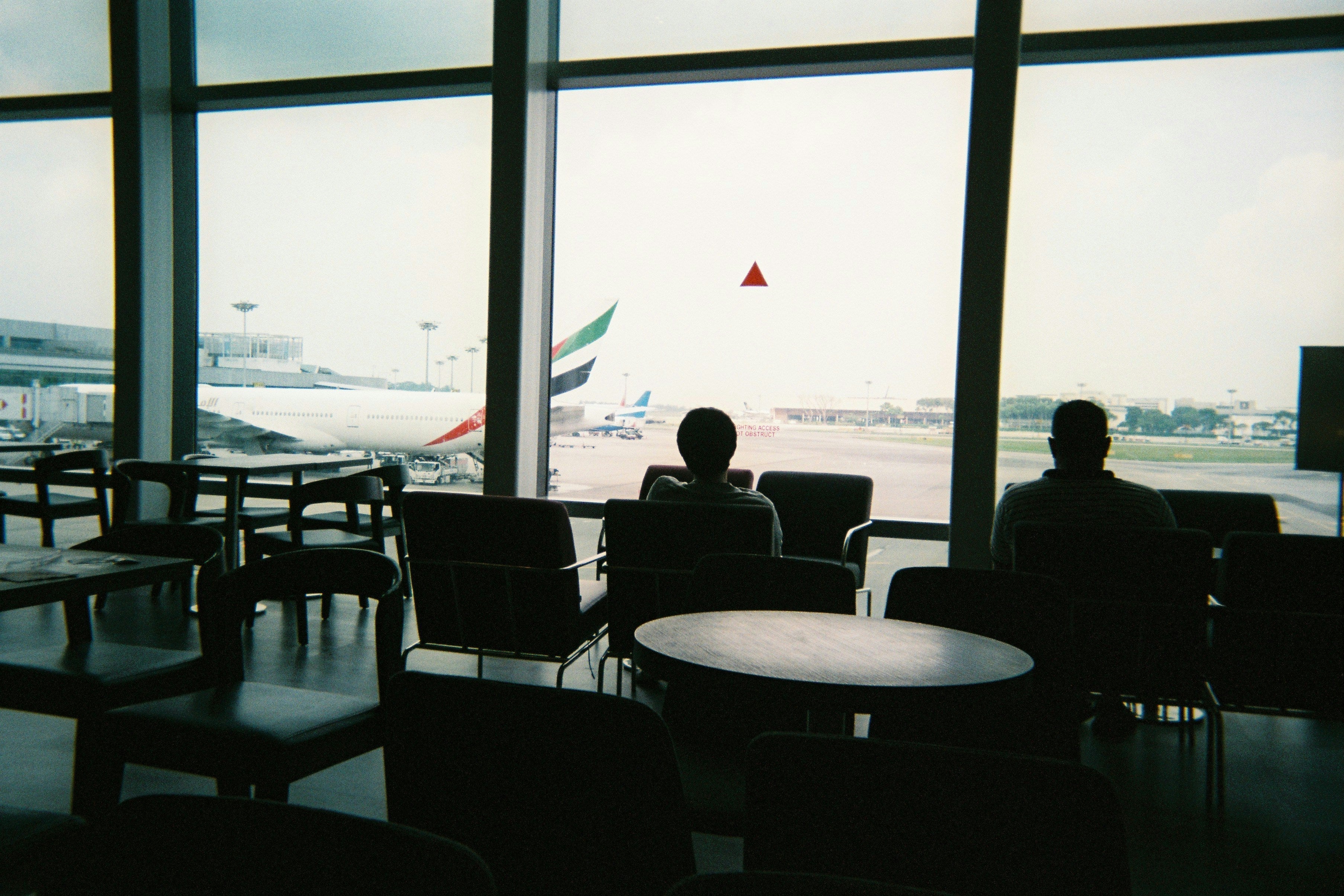 espace devant une vitre, il y a des fauteuils et des tables. On y voit des avions 