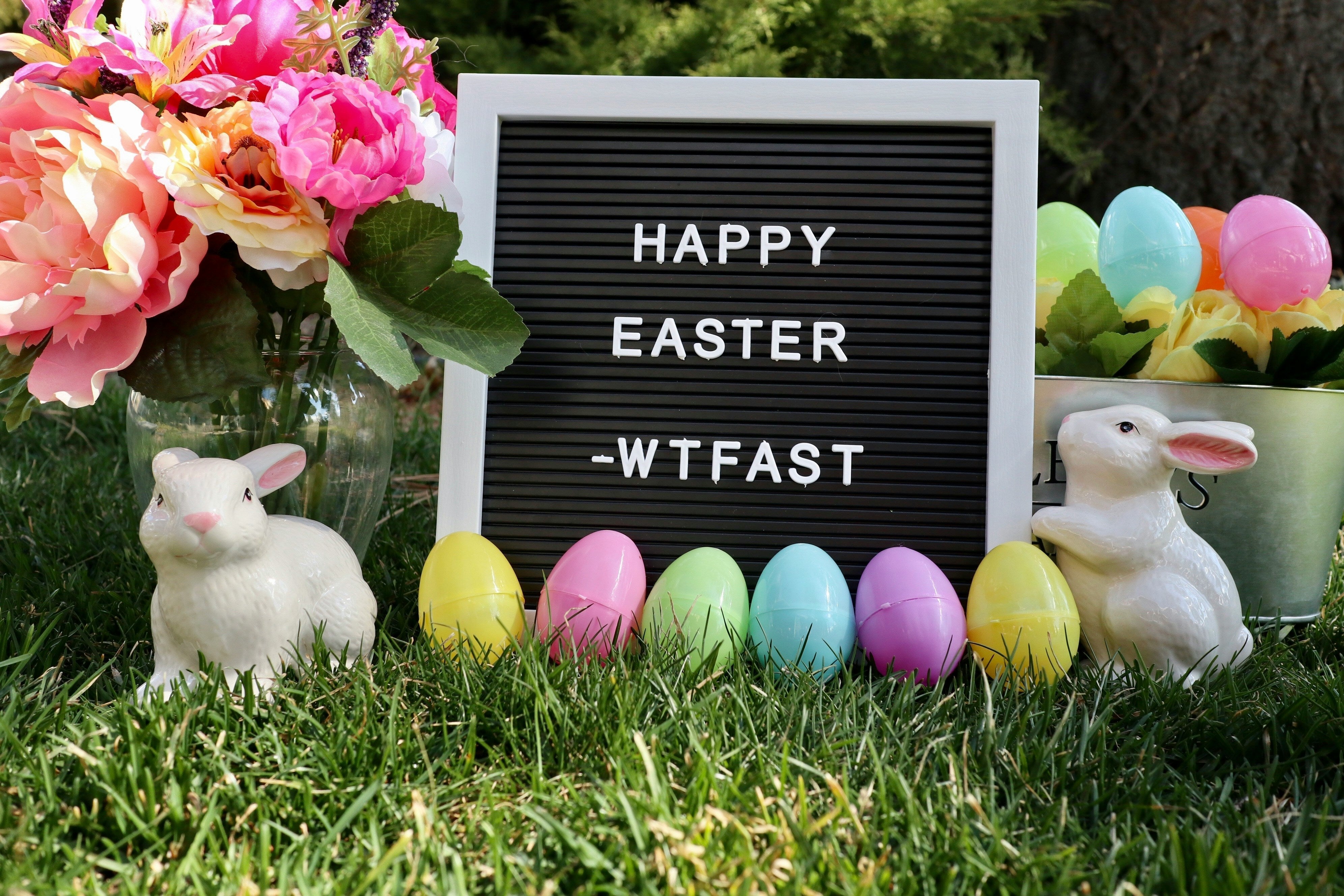 oeufs colorés, lapin, tableau avec écrit "happy easter" , des fleurs roses, sur l'herbe